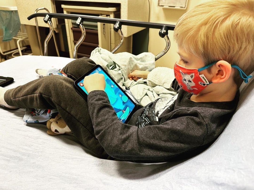 My son, Maverick (6), sitting in a hospital bed, playing a game on an iPad